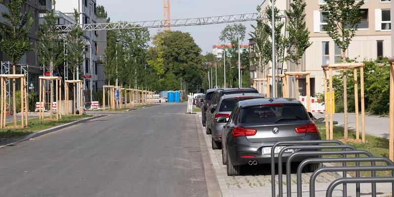 Ansicht der bereits fertiggestellten Otto-Meitinger-Straße mit Bäumen, Parkbuchten und Radlabstellmöglichkeiten.